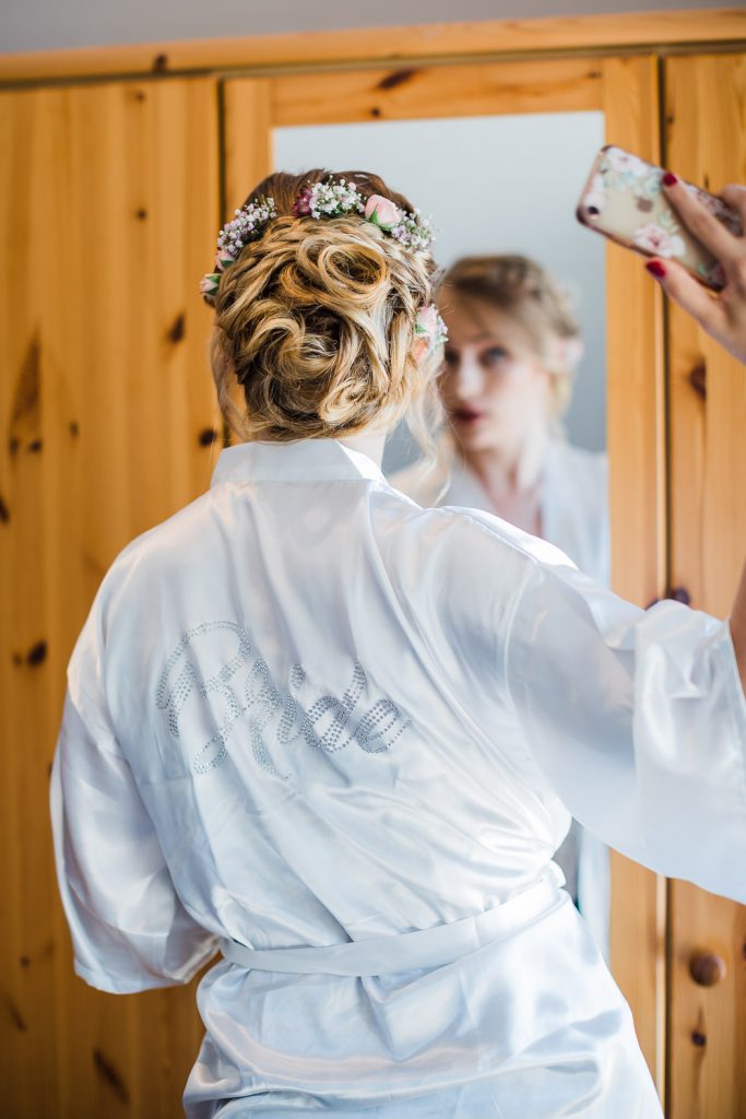 Braut betrachtet sich mit iPhone im Spiegel