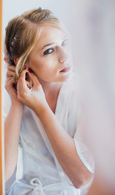 Braut steht vor dem Spiegel und steckt sich Ohrringe an