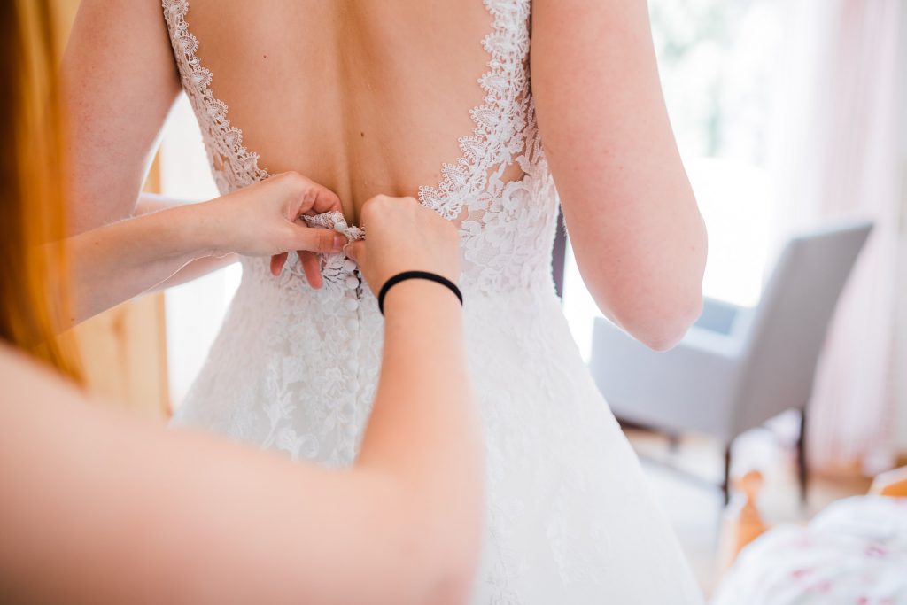 Trauzeugin schließt der Braut das Brautkleid