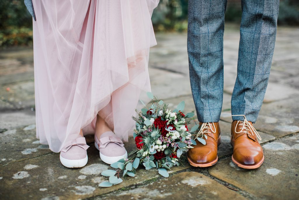 Detailaufnahme der Schuhe von Braut und Bräutigam mit dem Brautstrauß in der Mitte